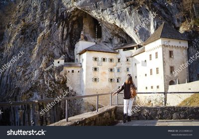 stock-photo-a-traveler-woman-stands-back-to-the-camera-and-enjys-view-of-predjama-castle-predjamski-grad-a-2111808113.jpg